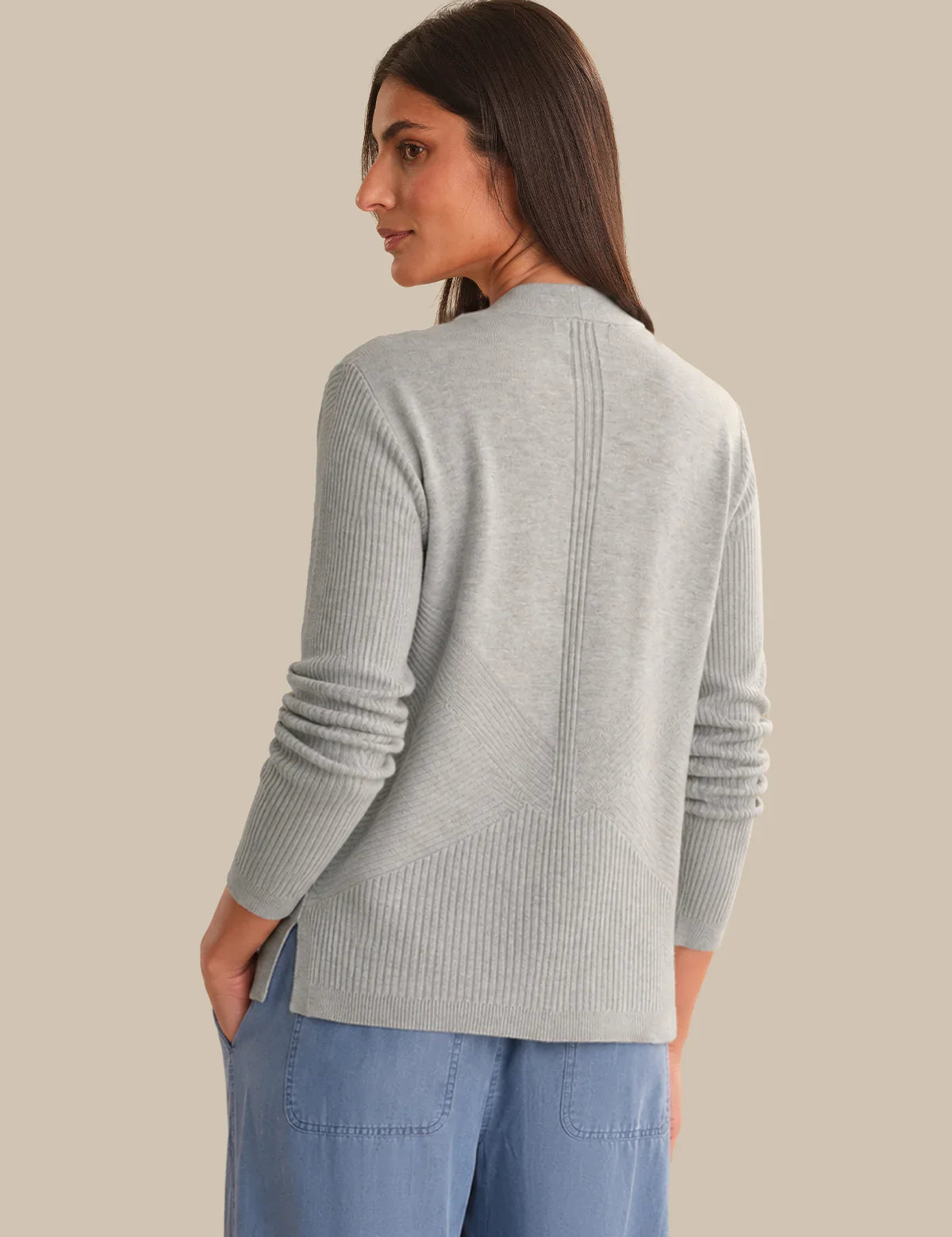 Woman wearing a light gray sweater and blue pants on a beige background
