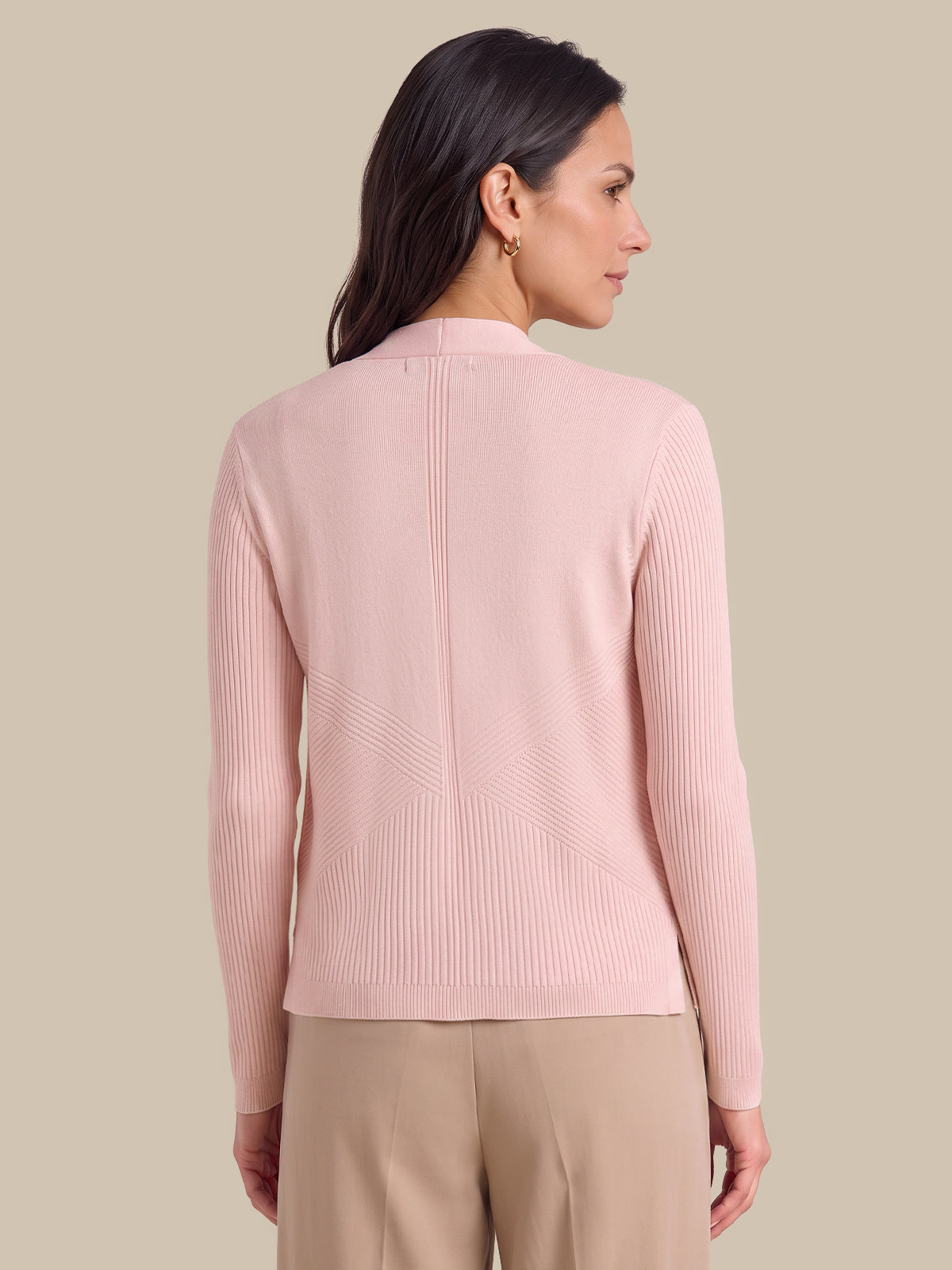 A woman shown from the back wearing a light pink ribbed knit cardigan with a high mock neck and beige trousers, set against a solid beige studio background.