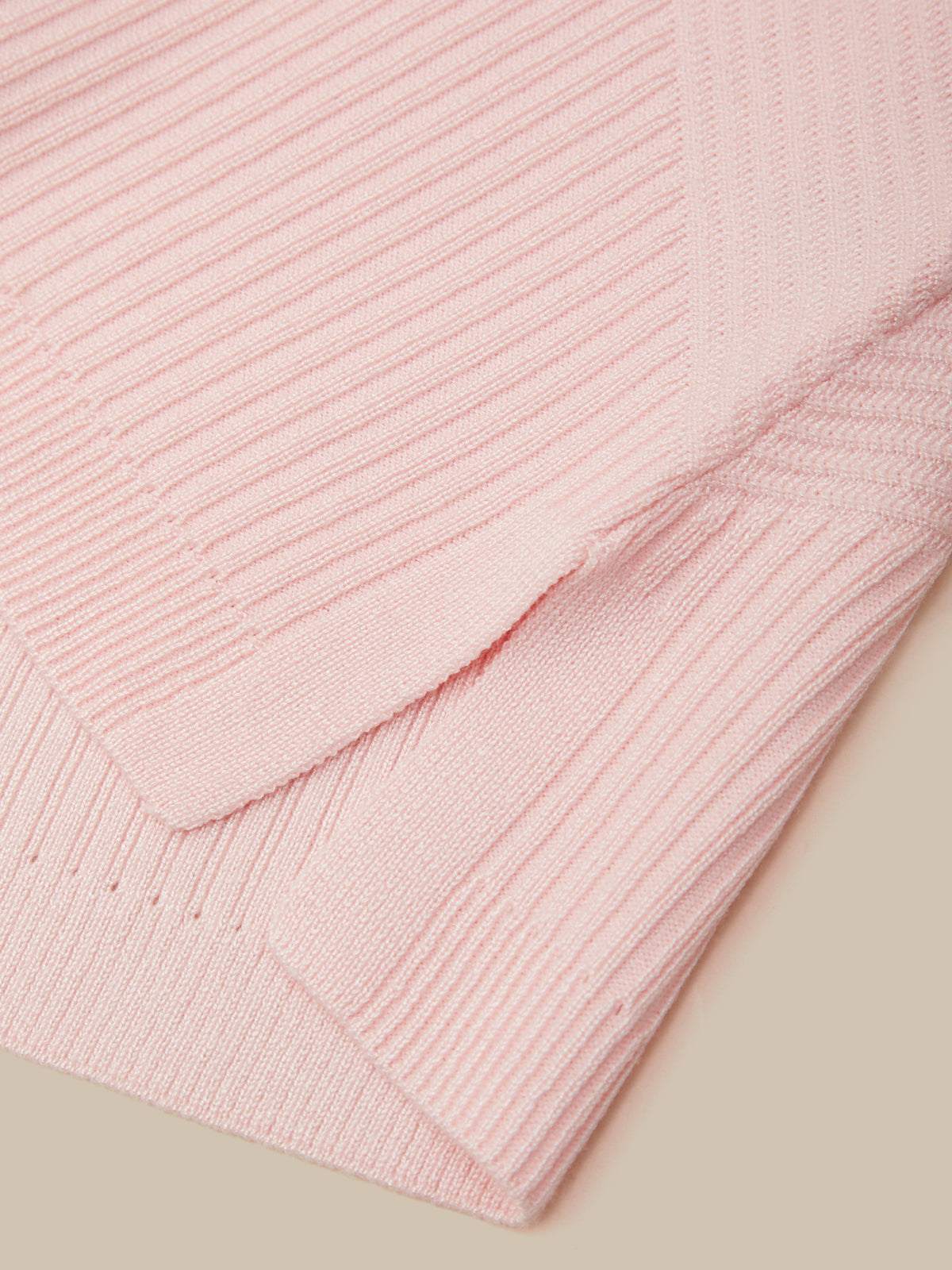 A close-up of a light pink ribbed knit fabric, showing the texture and folded edges against a solid beige background.