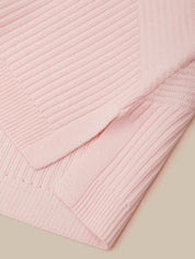 A close-up of a light pink ribbed knit fabric, showing the texture and folded edges against a solid beige background.
