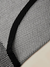 Close-up of a gray and white herringbone patterned fabric with a black stitched border, shown against a light beige background.