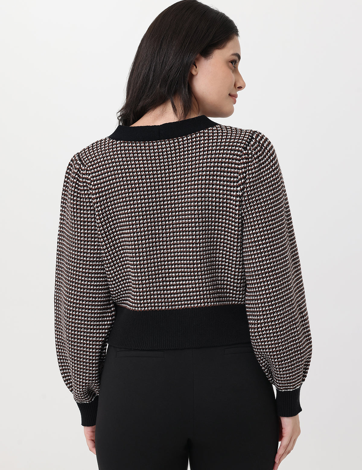 Woman wearing a chocolate and white patterned cardigan with long sleeves on a light gray background