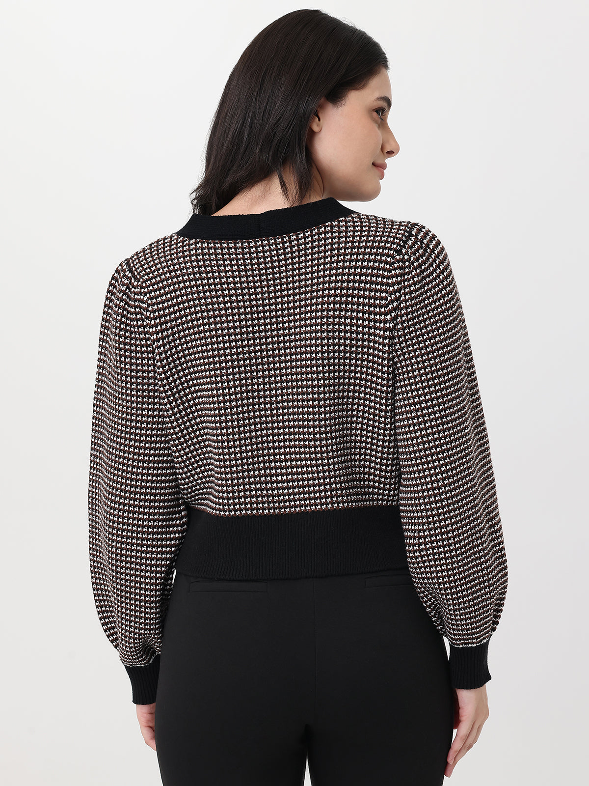 Woman wearing a chocolate and white patterned cardigan with long sleeves on a light gray background