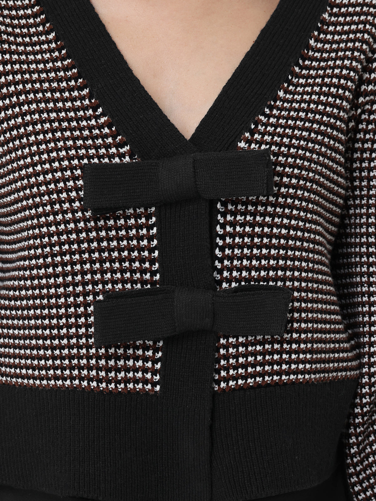 Close-up of a chocolate and white patterned cardigan with a black bow detail.