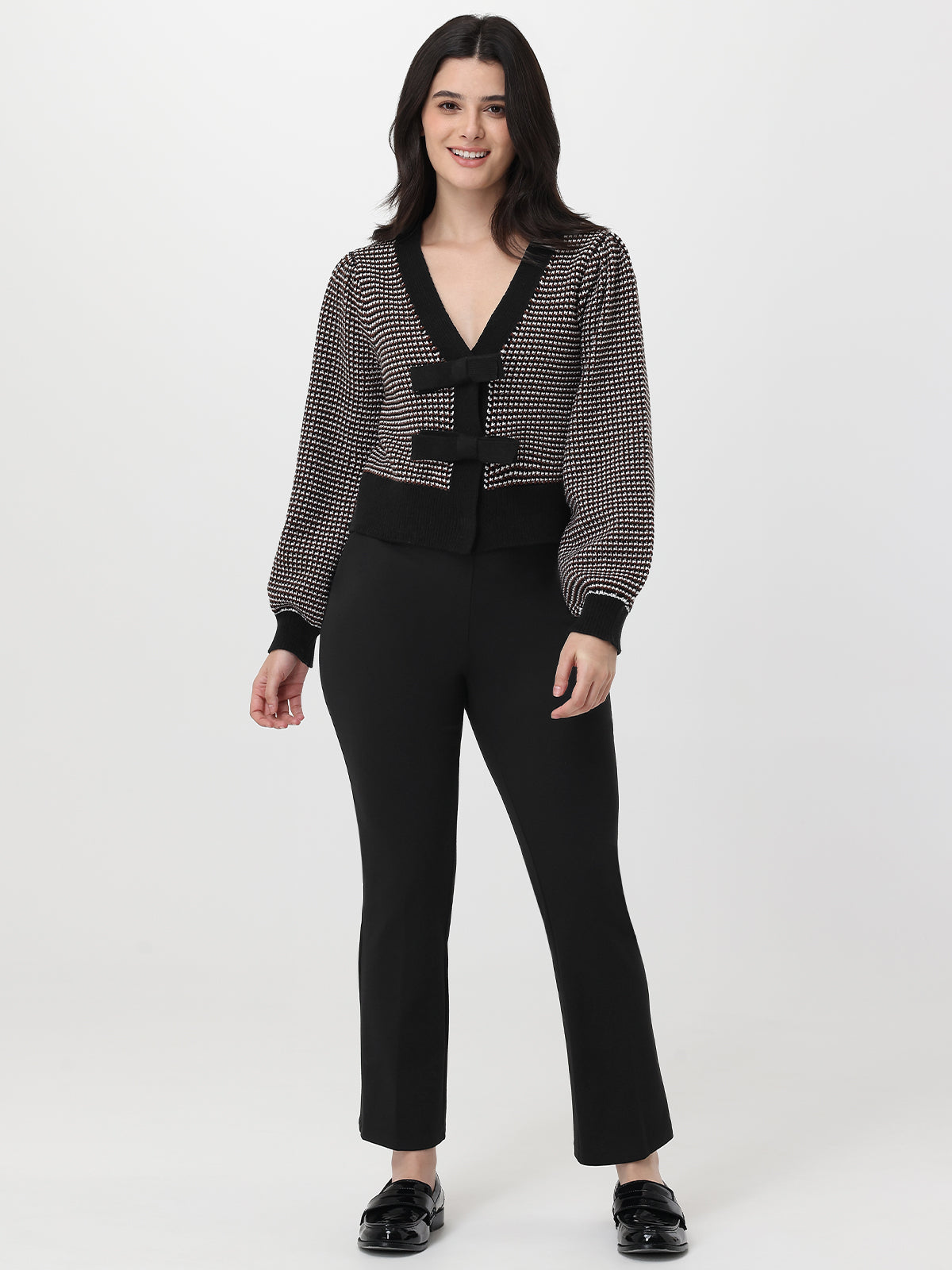 Woman wearing a chocolate and white patterned cardigan with a black skirt on a white background