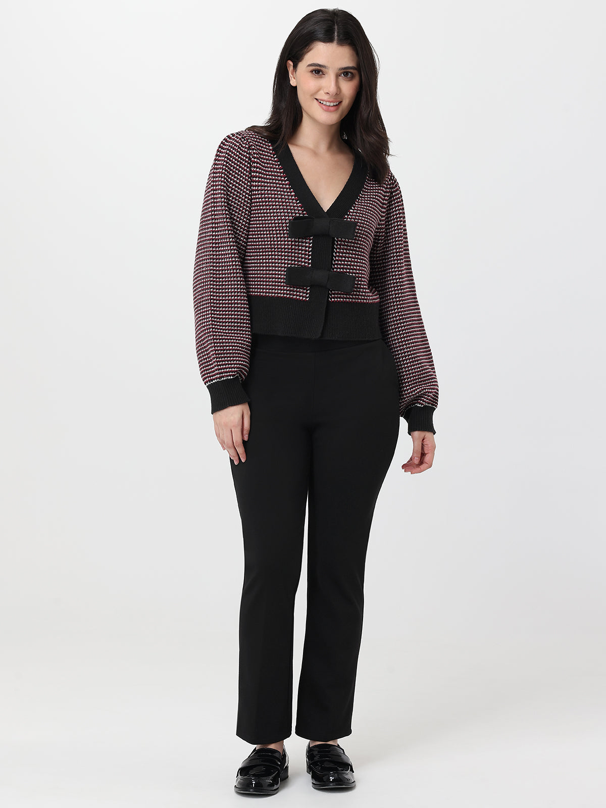 Woman wearing a patterned cardigan over a deep garnet top and pants on a white background