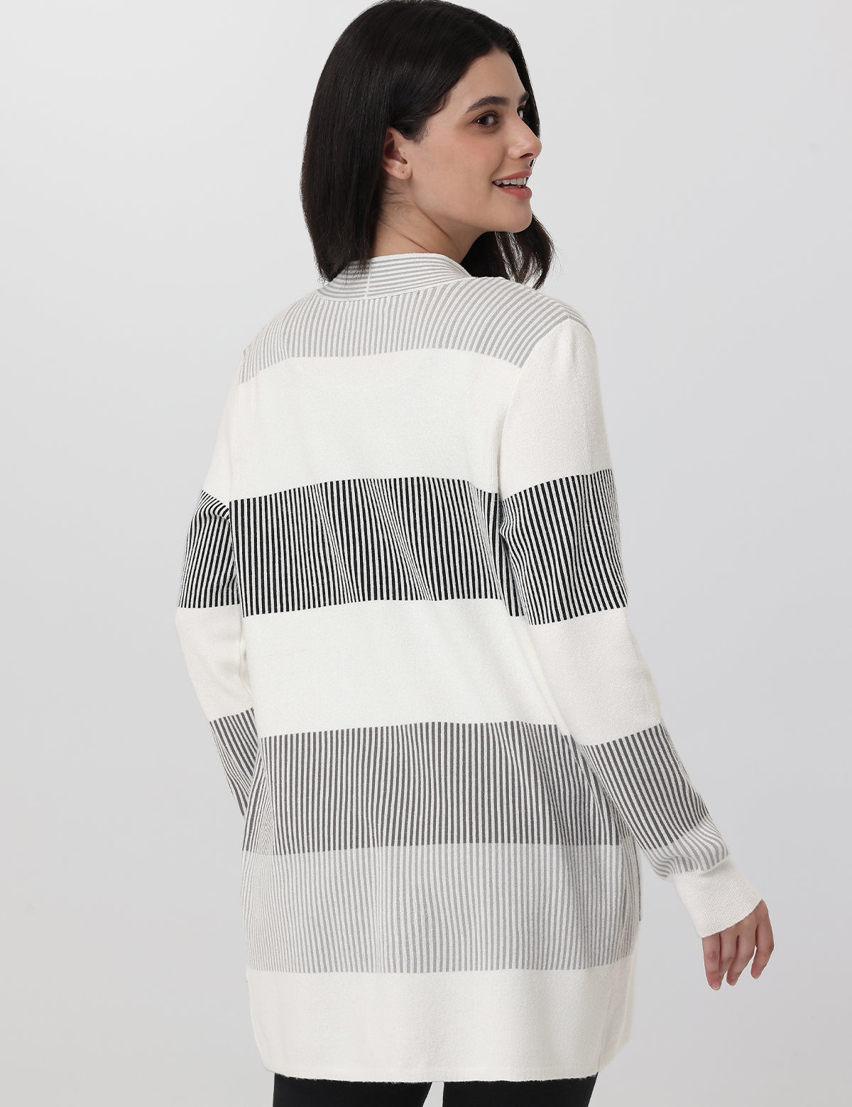 Woman wearing a long, striped shirt with vertical black and white stripes on a plain background