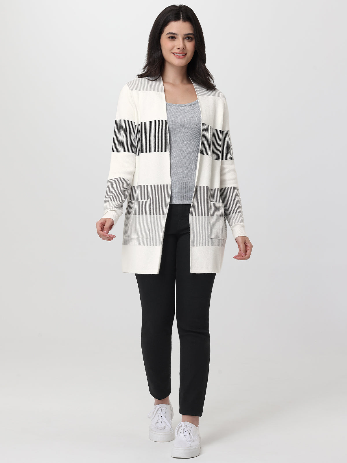 Woman wearing a striped cardigan over a gray top and black pants on a white background