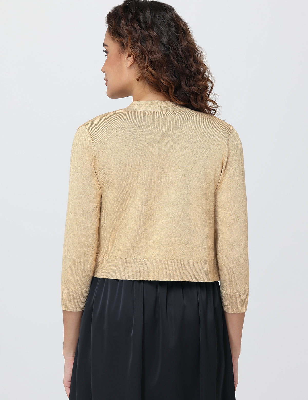 Woman wearing a beige cardigan over a black outfit on a light gray background