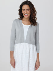 Woman wearing a gray cardigan over a white dress with a subtle pattern on a plain background