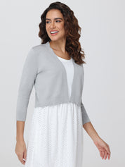 Woman wearing a gray cardigan over a white dress with a plain background