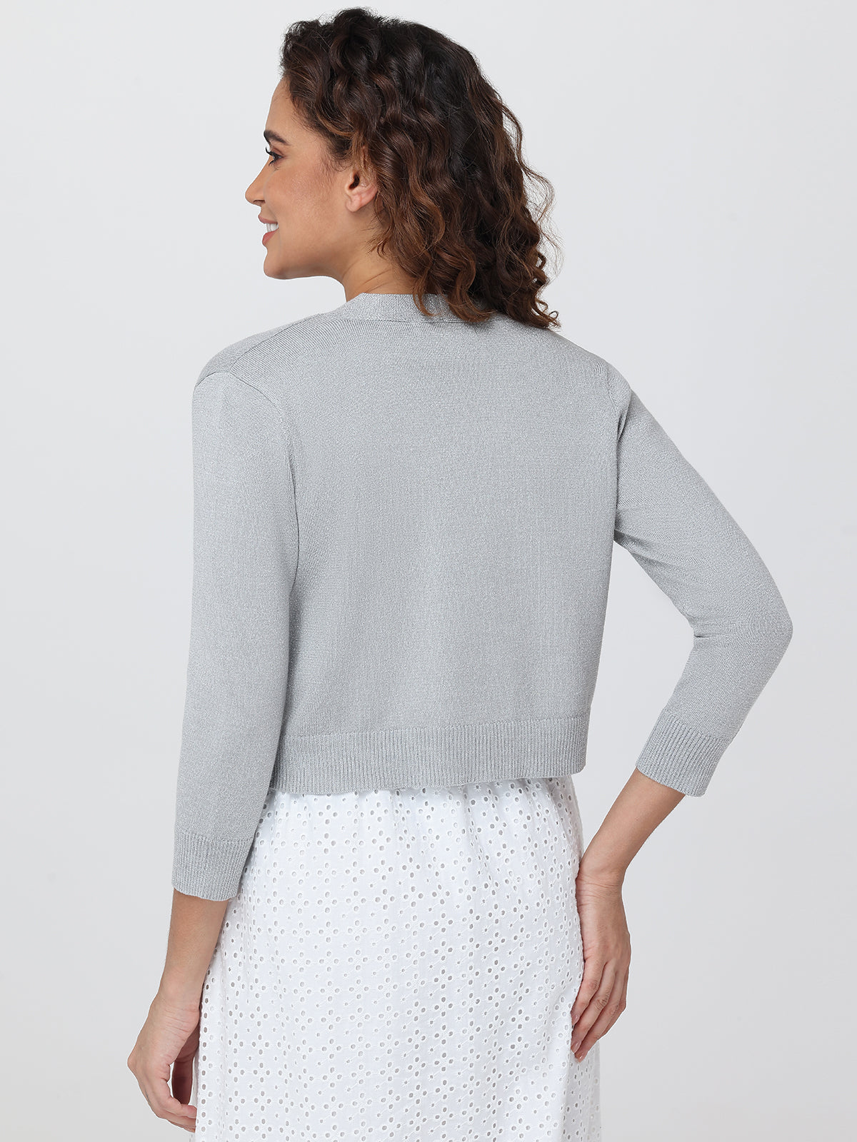 Woman wearing a light gray cardigan over a white dress with a subtle pattern on a plain background