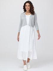 Woman wearing a gray cardigan over a white dress with lace details on a white background