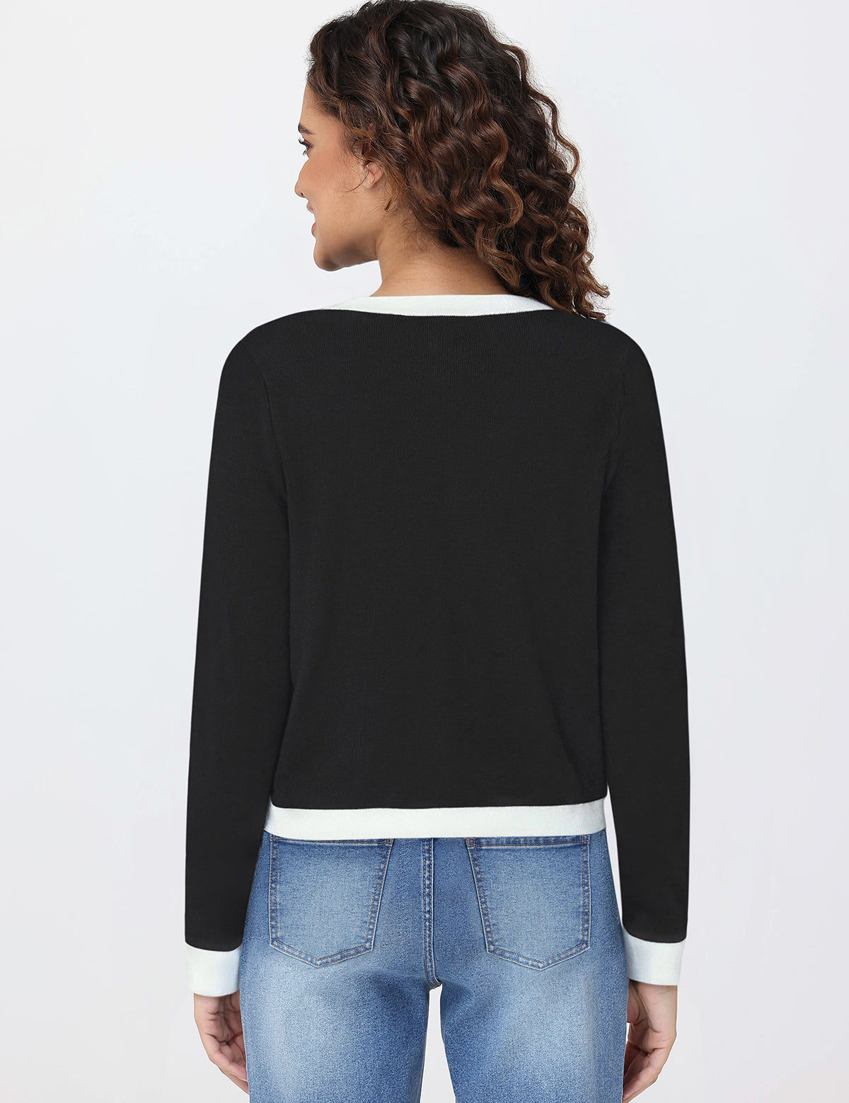 Woman wearing a black cardigan with white trim and blue jeans on a light gray background