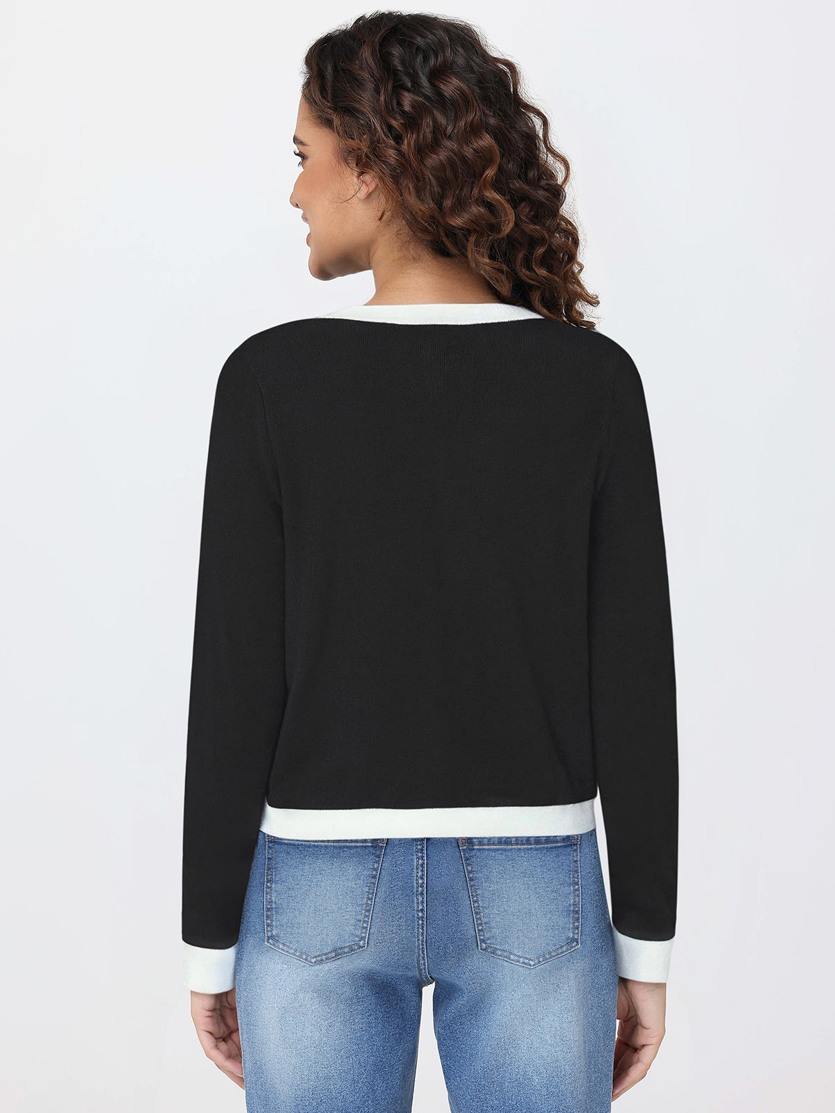 Woman wearing a black cardigan with white trim and blue jeans on a light gray background