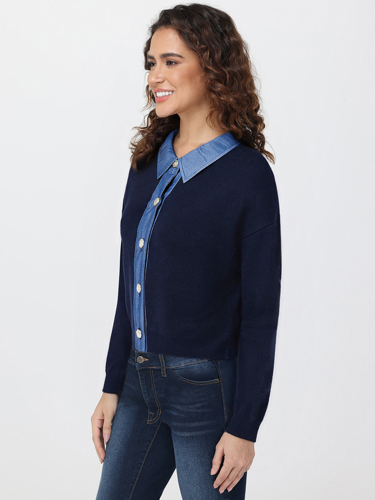 Woman wearing a navy cardigan over a denim shirt with jeans on a white background