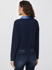 Person wearing a navy sweater with a blue collar and dark jeans on a light gray background