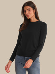 A woman modeling a black long-sleeve crewneck sweater paired with blue jeans, set against a solid beige studio background.