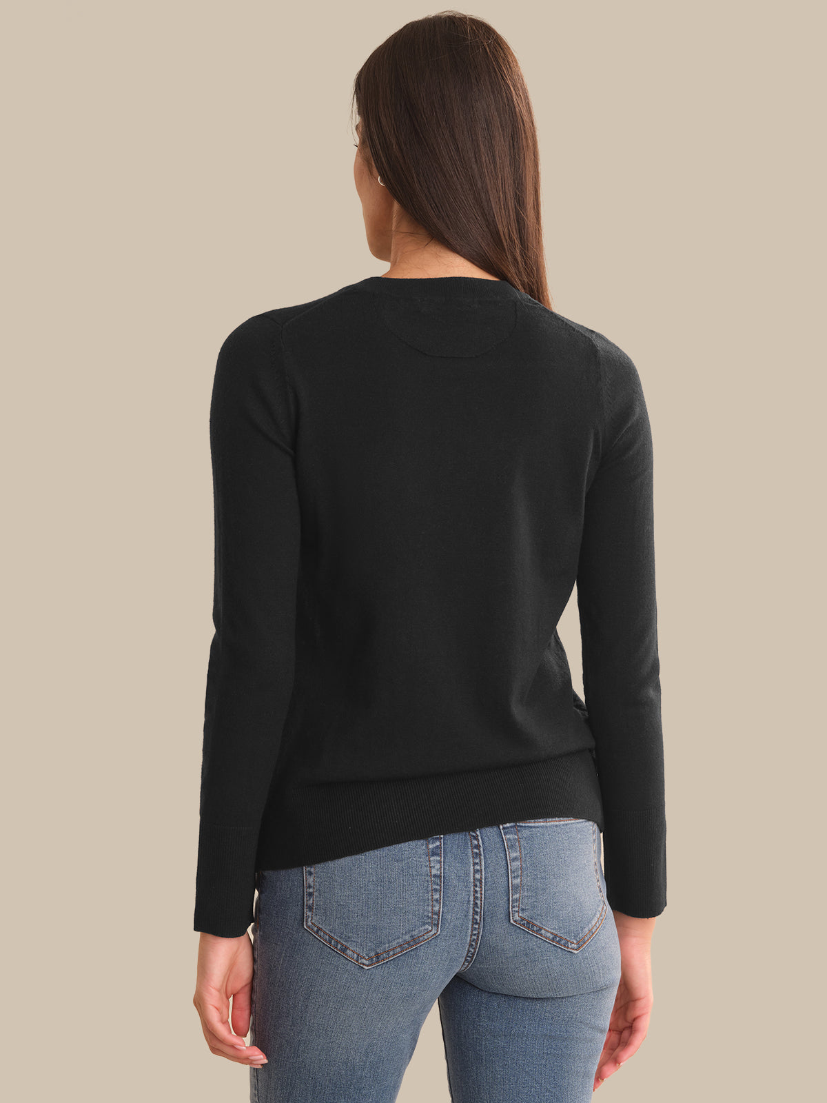 A woman shown from the back wearing a black long-sleeve knit sweater and light blue jeans against a solid beige background.