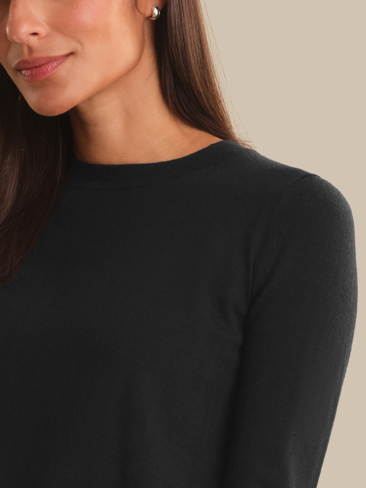 Close-up of a woman wearing a plain black long-sleeve crewneck top against a warm beige background.