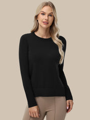 A woman modeling a black long-sleeve crewneck sweater paired with beige pants, set against a solid beige background.