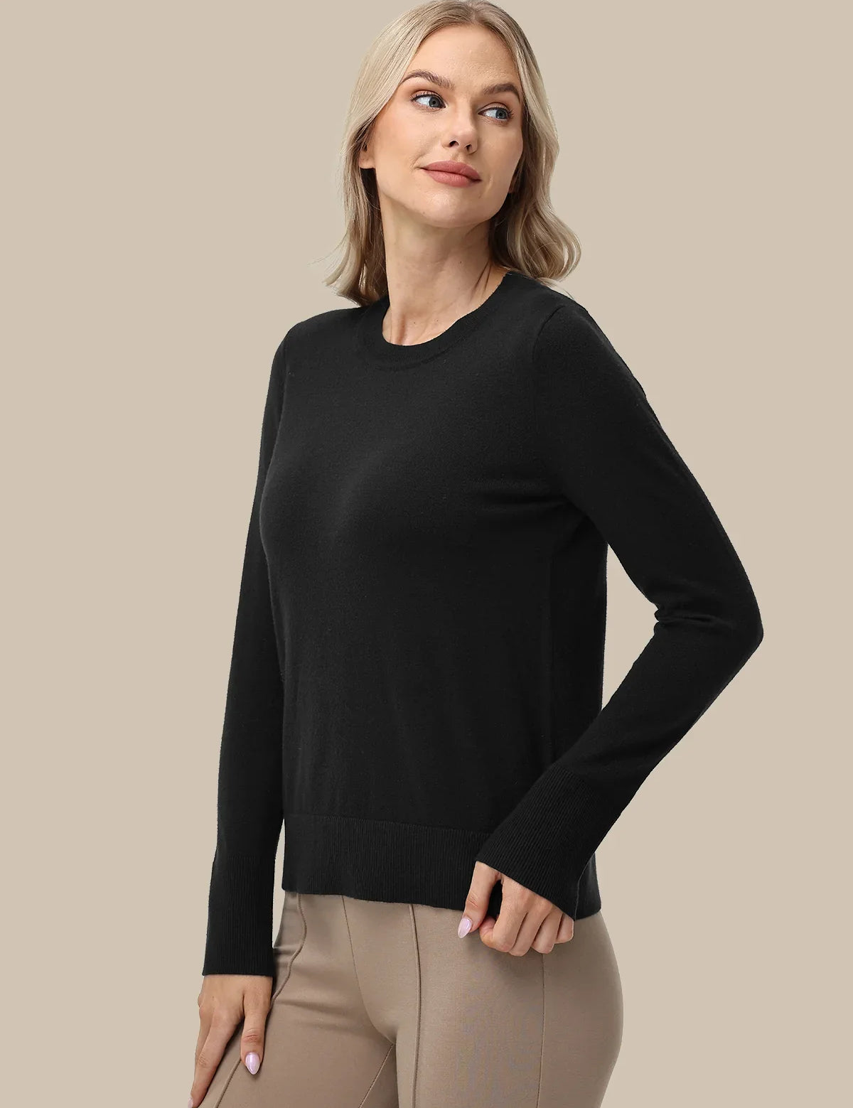 A woman modeling a black long-sleeve crewneck sweater paired with beige pants, set against a solid beige studio background.