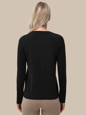 A woman viewed from the back wearing a black long-sleeve crewneck top and beige pants, set against a solid beige background.
