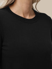 Close-up of a person wearing a plain black crew-neck top against a light beige background.
