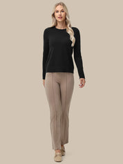 A woman modeling a black long-sleeve crewneck sweater and beige straight-leg trousers against a solid beige background.