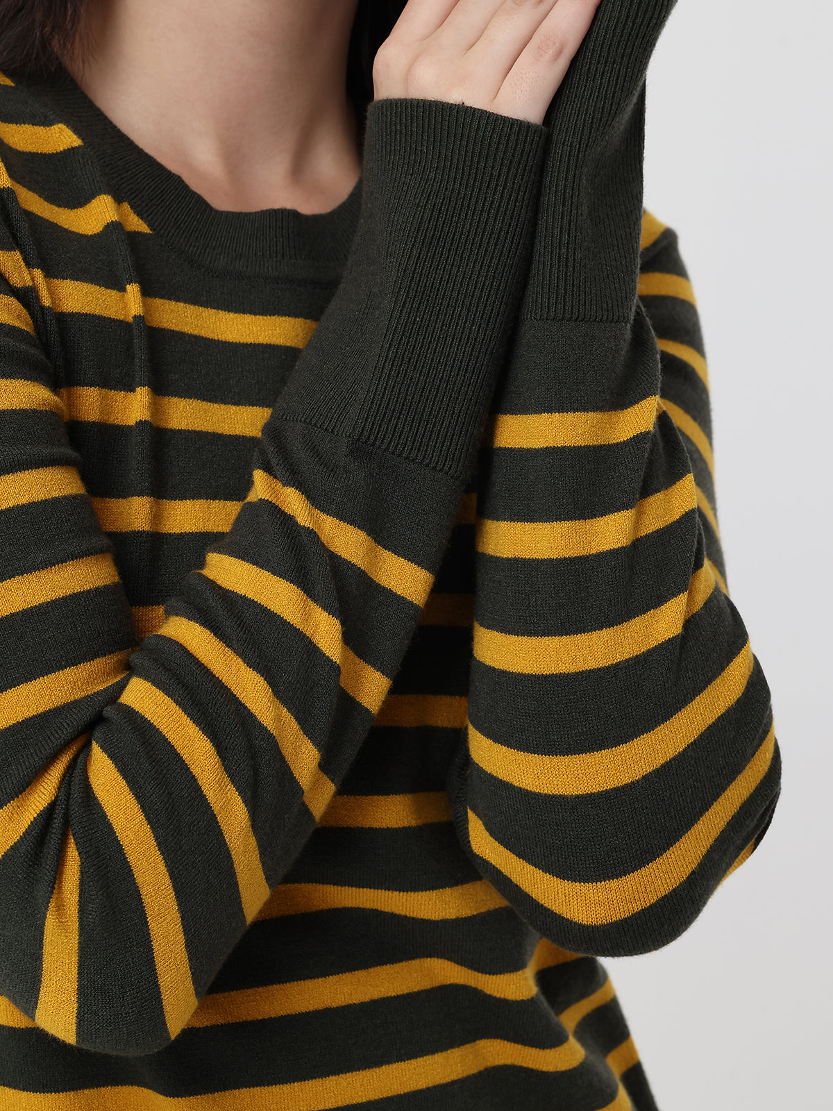 Close-up of a black and mustard yellow striped sweater on a plain background