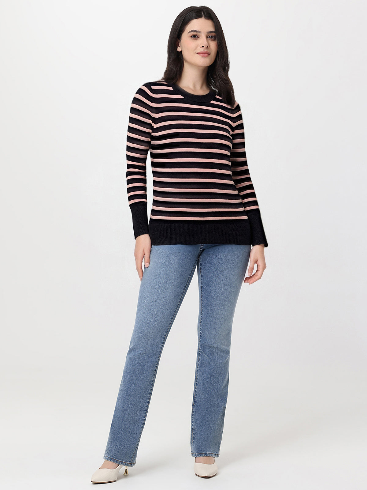Woman wearing a black and pink striped sweater with blue jeans on a white background