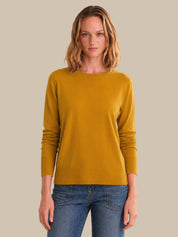 Woman wearing a mustard yellow sweater and blue jeans against a beige background