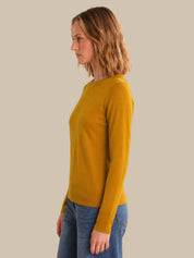 Woman wearing a mustard yellow long-sleeve top against a plain background