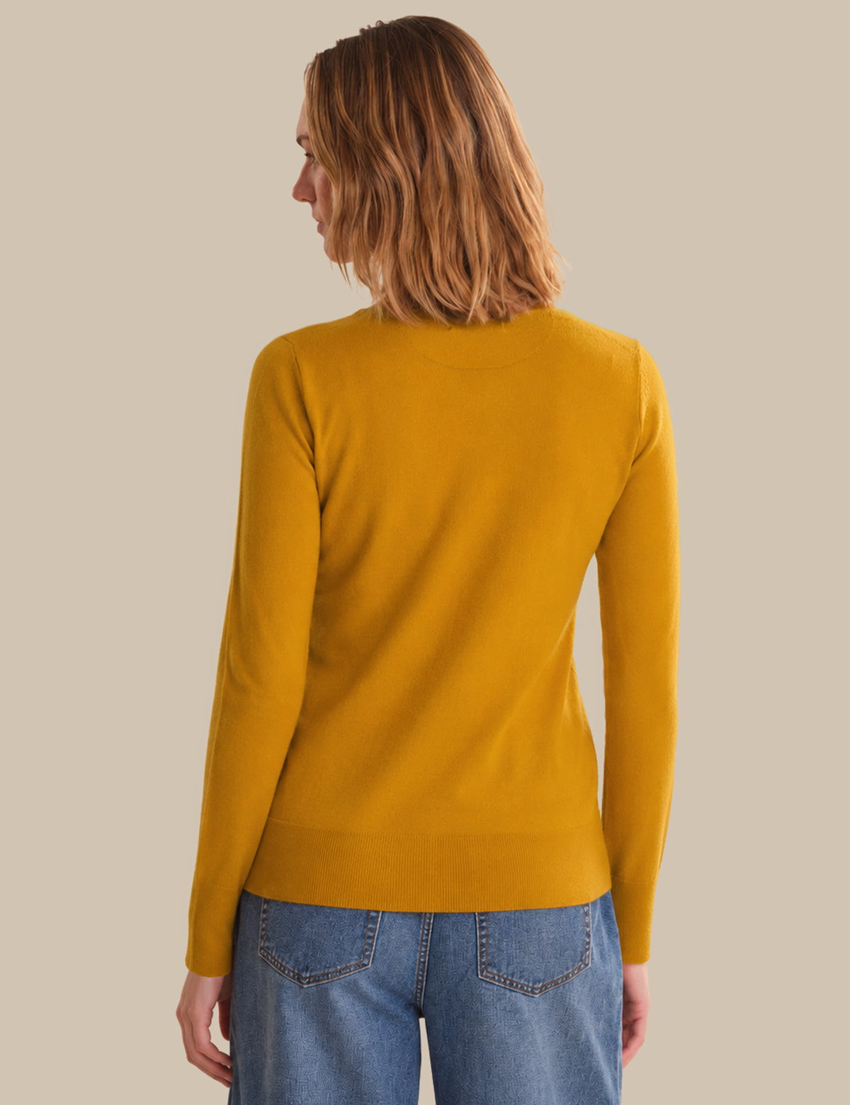 Person wearing a mustard yellow sweater and blue jeans on a beige background