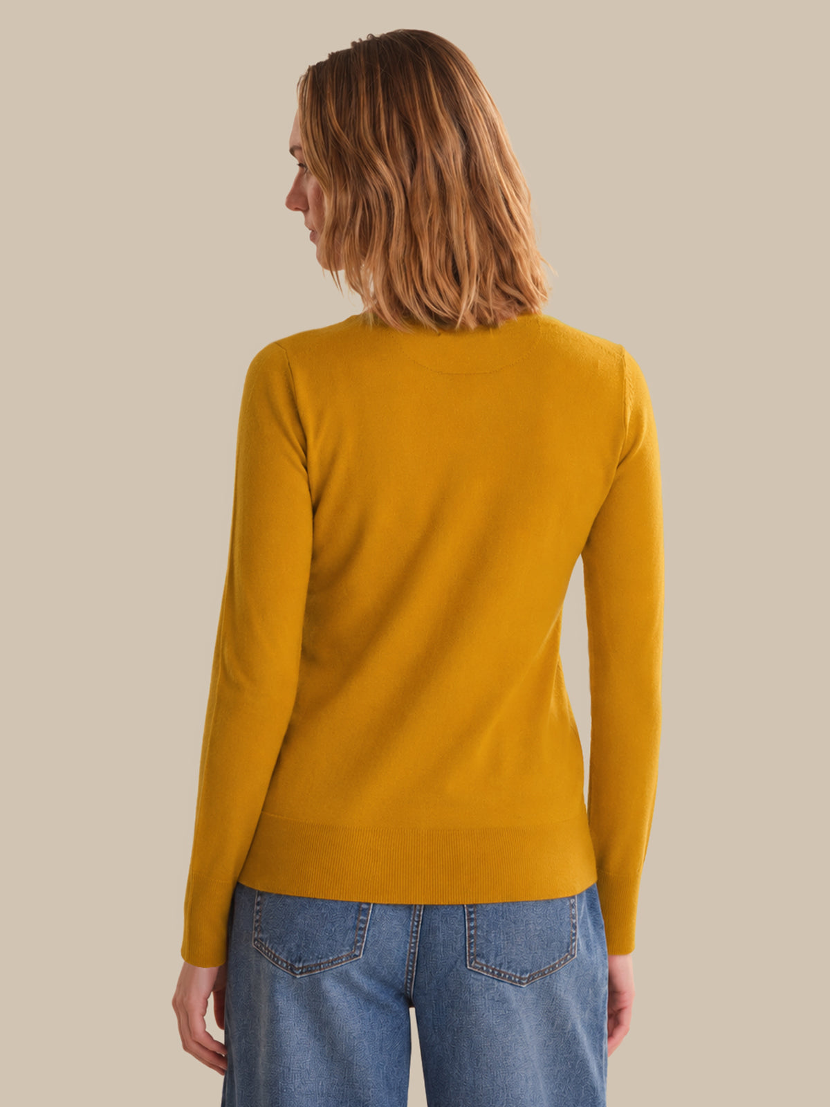 Person wearing a mustard yellow sweater and blue jeans on a beige background