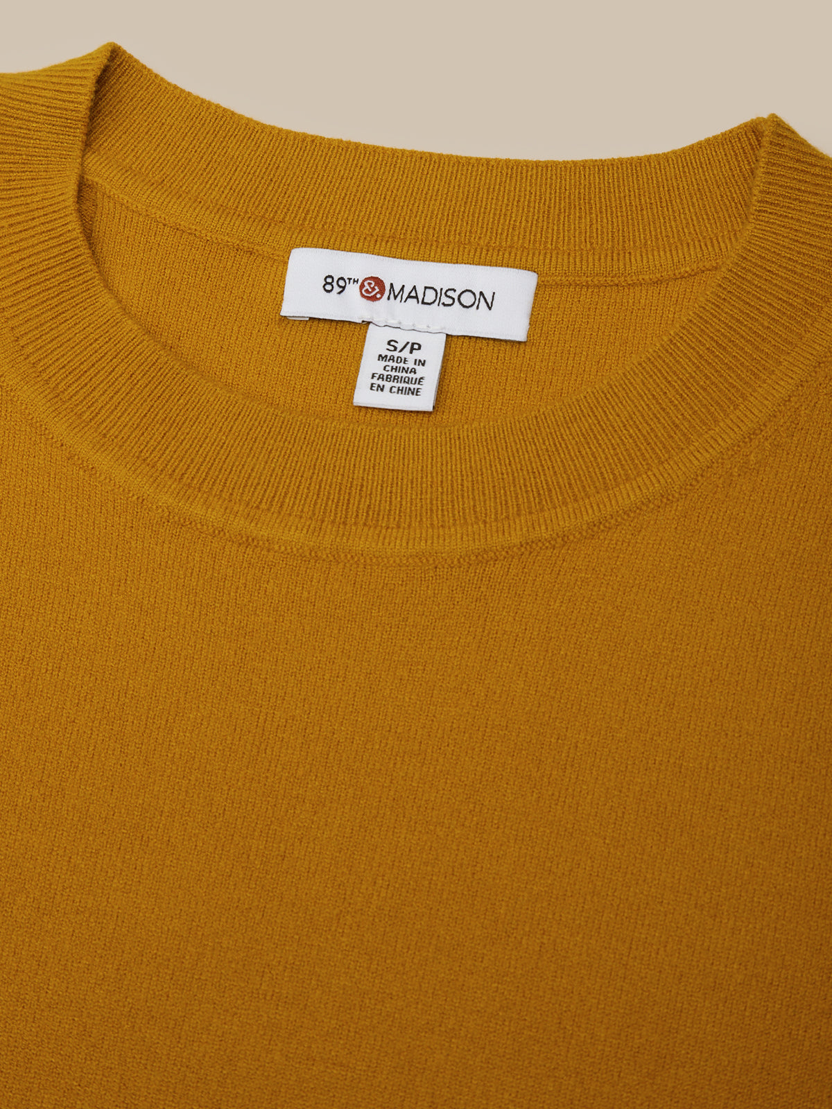 Close-up of a mustard yellow sweater with a brand label on a beige background