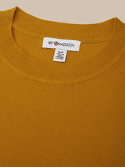 Close-up of a mustard yellow sweater with a brand label on a beige background