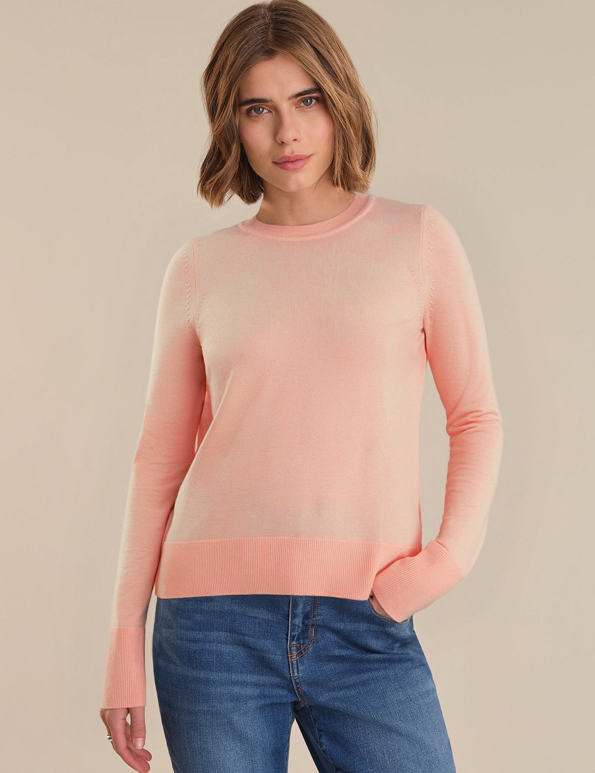 Woman wearing a pink sweater and blue jeans on a beige background