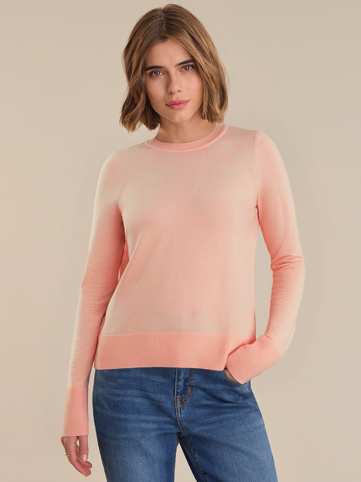 Woman wearing a pink sweater and blue jeans on a beige background