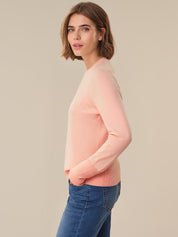 Woman wearing a pink sweater and blue jeans against a beige background