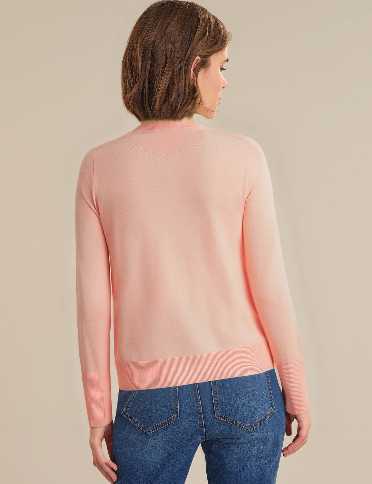Woman wearing a light pink sweater and blue jeans on a beige background