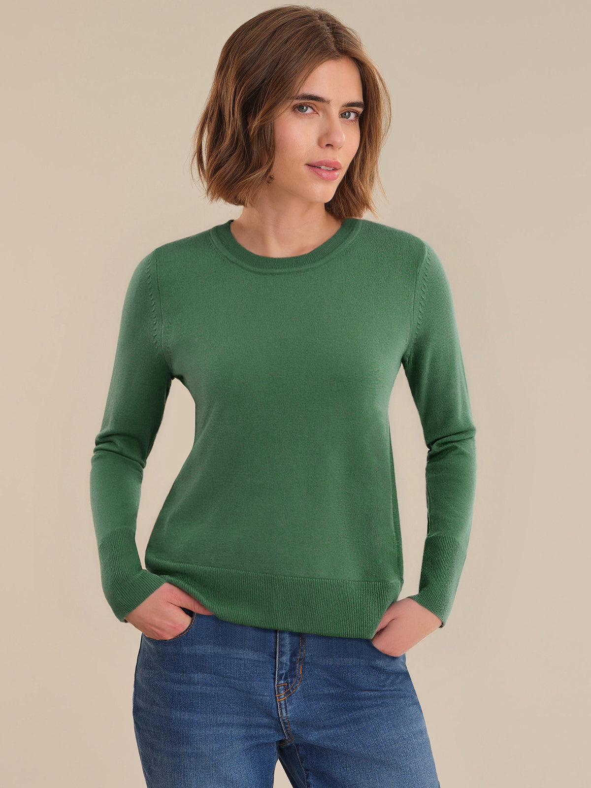 Woman wearing a green sweater and blue jeans against a beige background
