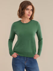 Woman wearing a green sweater and blue jeans against a beige background