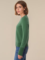 Woman wearing a green sweater and blue jeans against a beige background