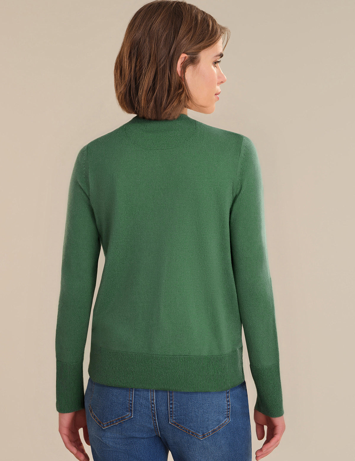 Person wearing a green sweater and blue jeans on a beige background