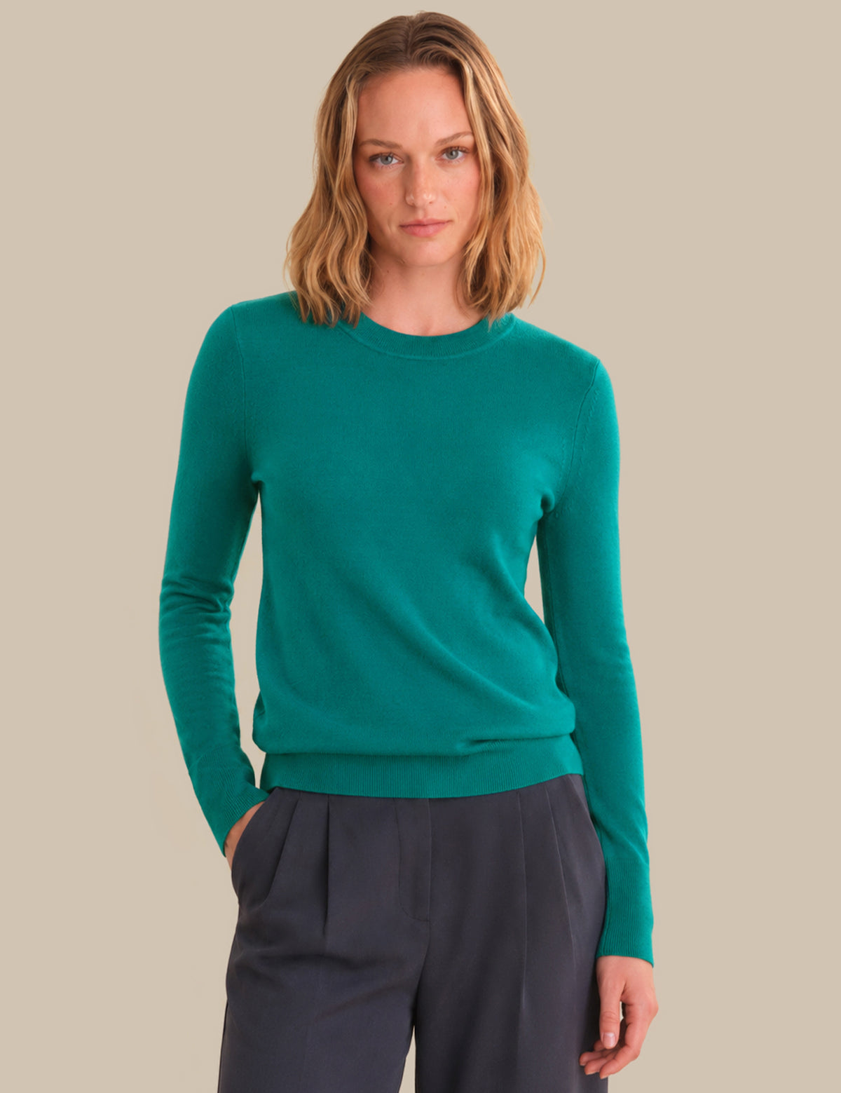 Woman wearing a teal sweater and dark pants against a beige background