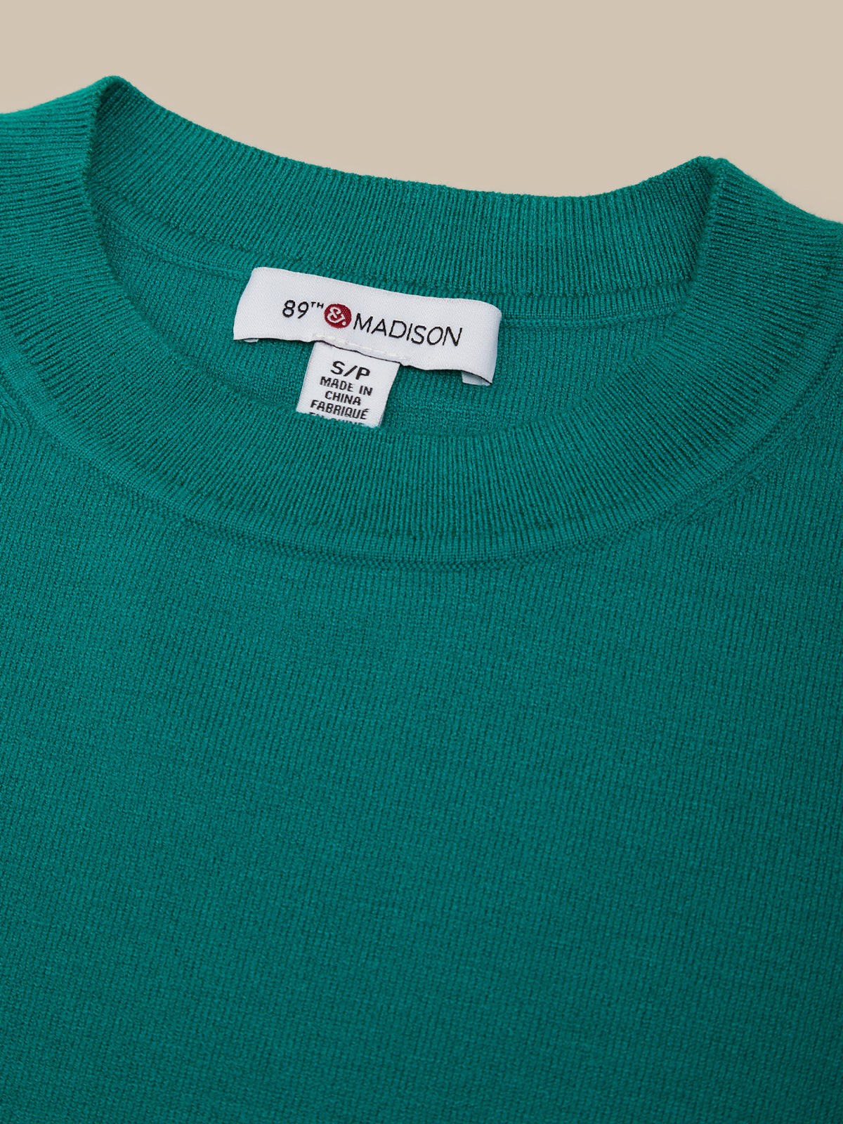 Close-up of a teal sweater with a brand label on a beige background