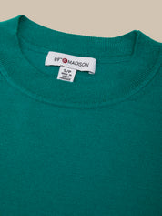 Close-up of a teal sweater with a brand label on a beige background