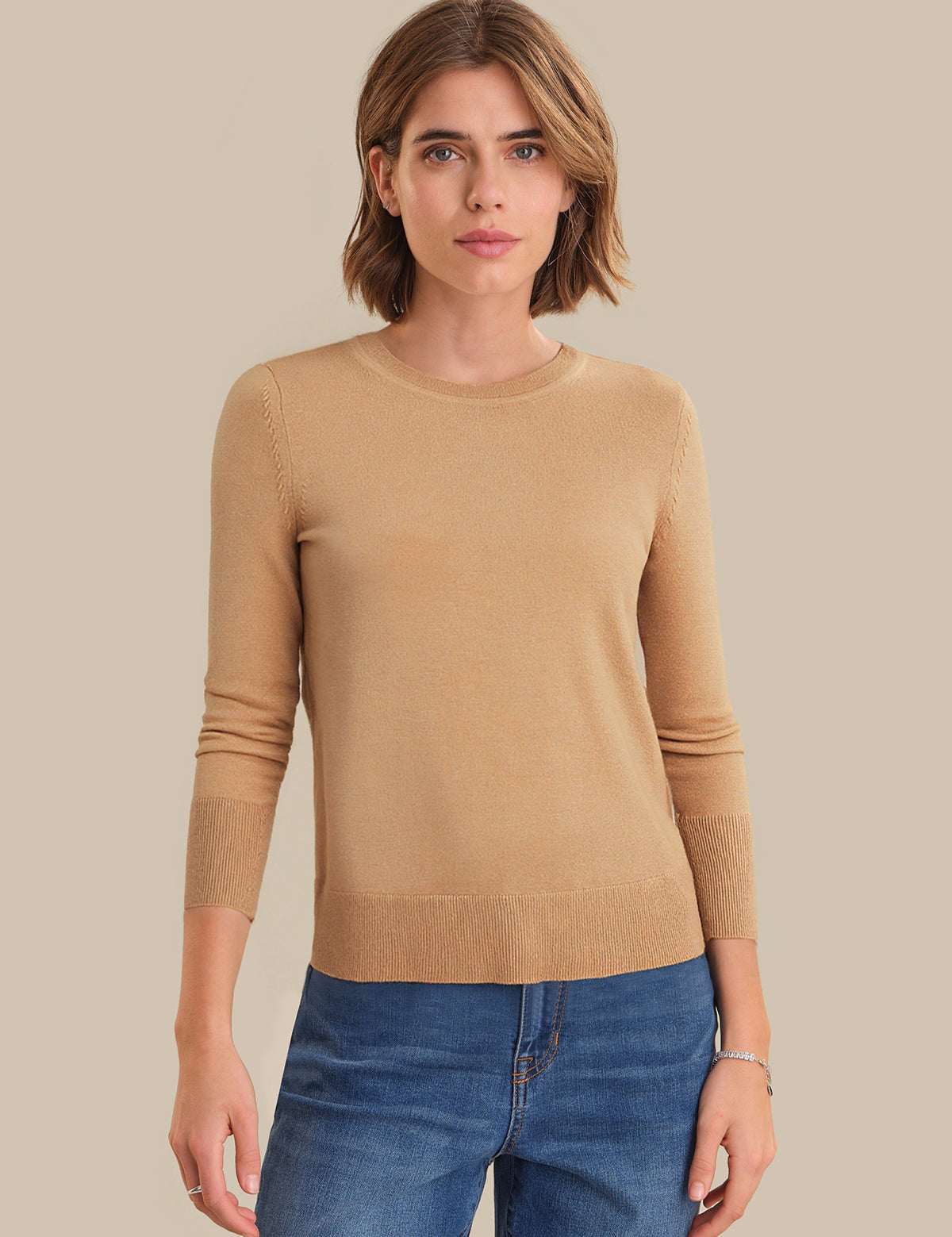 Woman wearing a beige sweater and blue jeans on a beige background