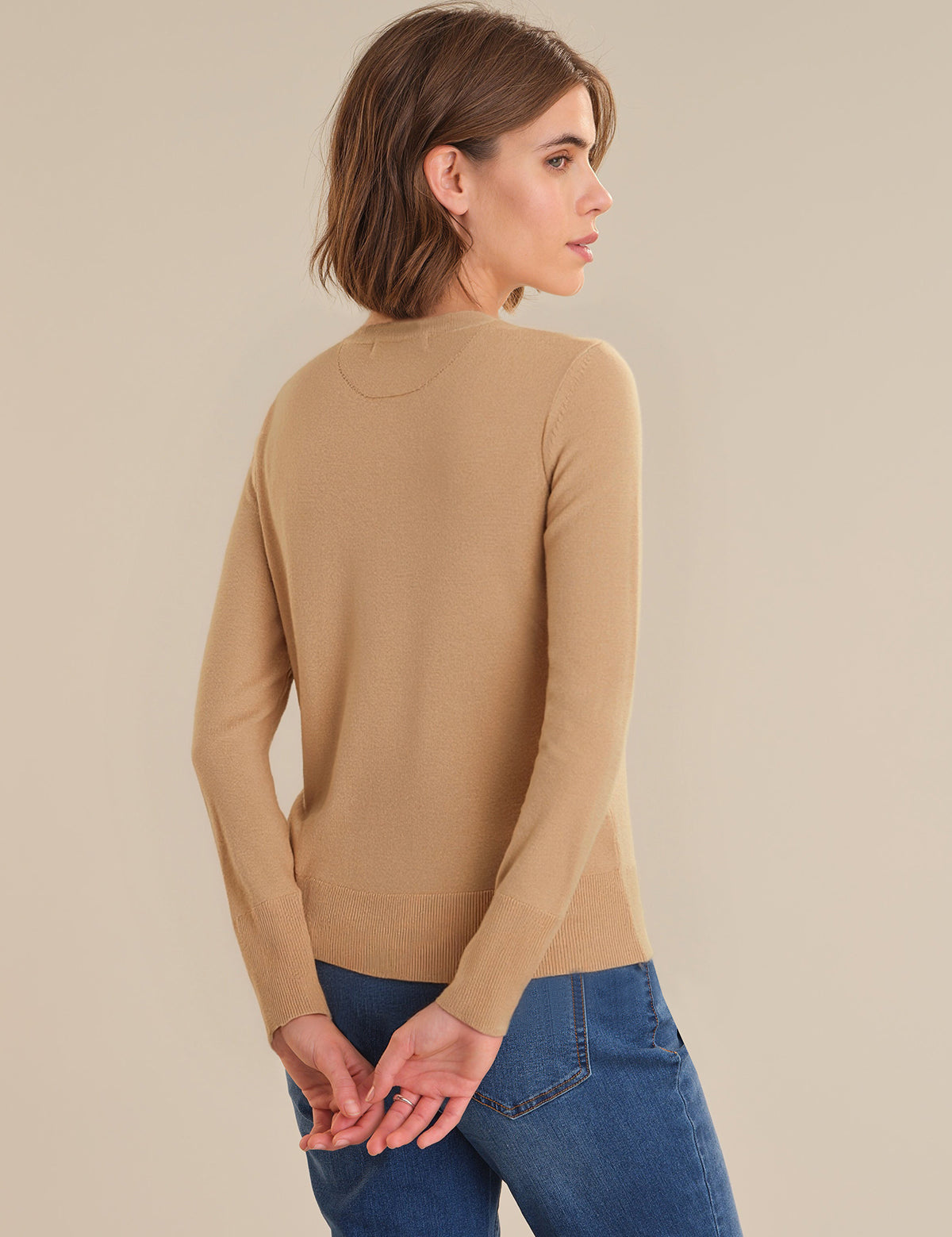 Woman wearing a beige long-sleeve top and blue jeans on a beige background
